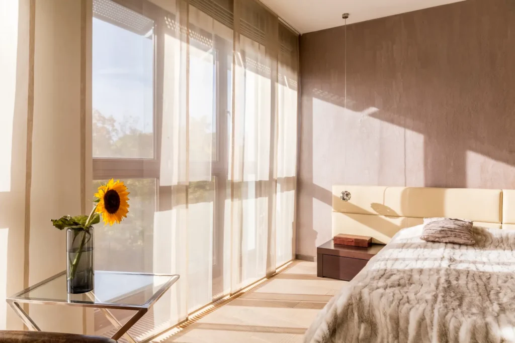 Beige hotel room with motorized drapery over the floor-to-ceiling windows.